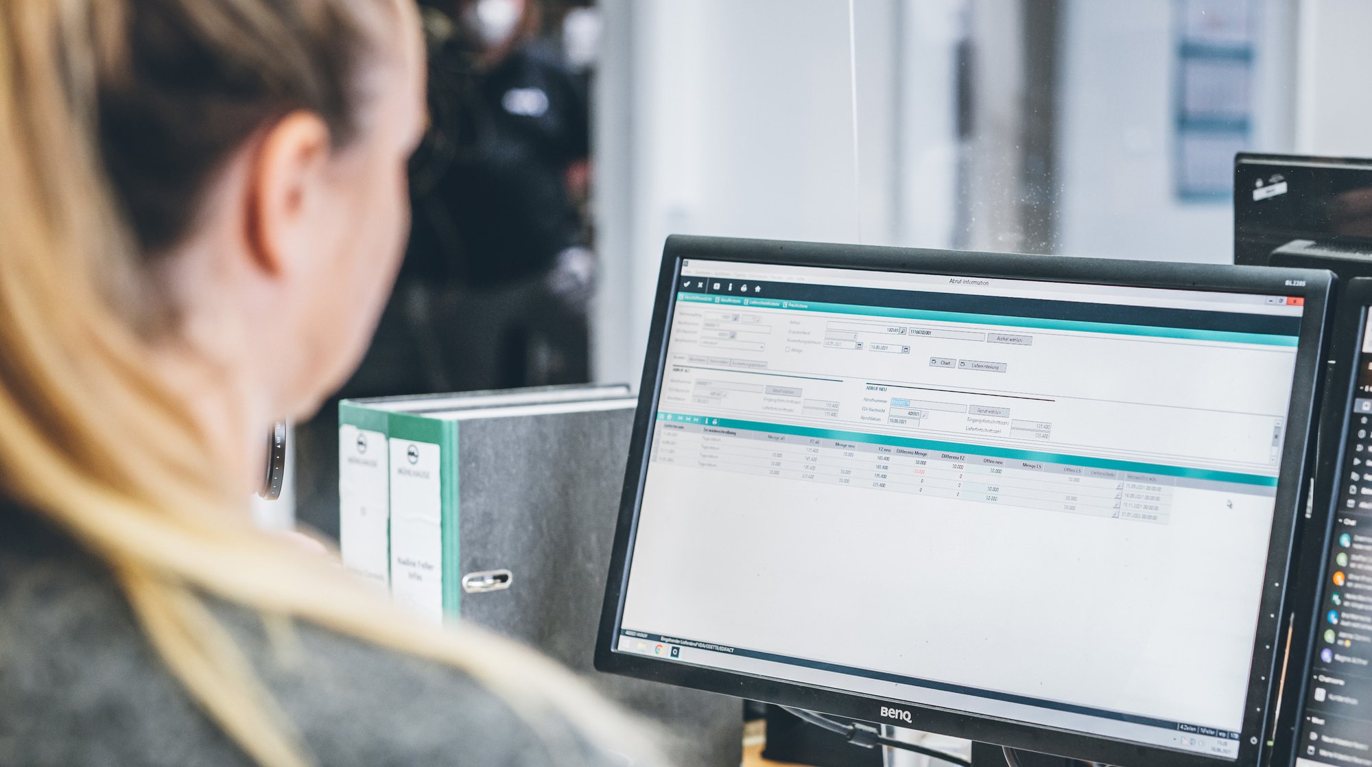 Person vor einem Computerbildschirm mit geöffneter Benutzeroberfläche und Tabellenansicht. Person vor einem Computerbildschirm mit geöffneter Benutzeroberfläche und Tabellenansicht.